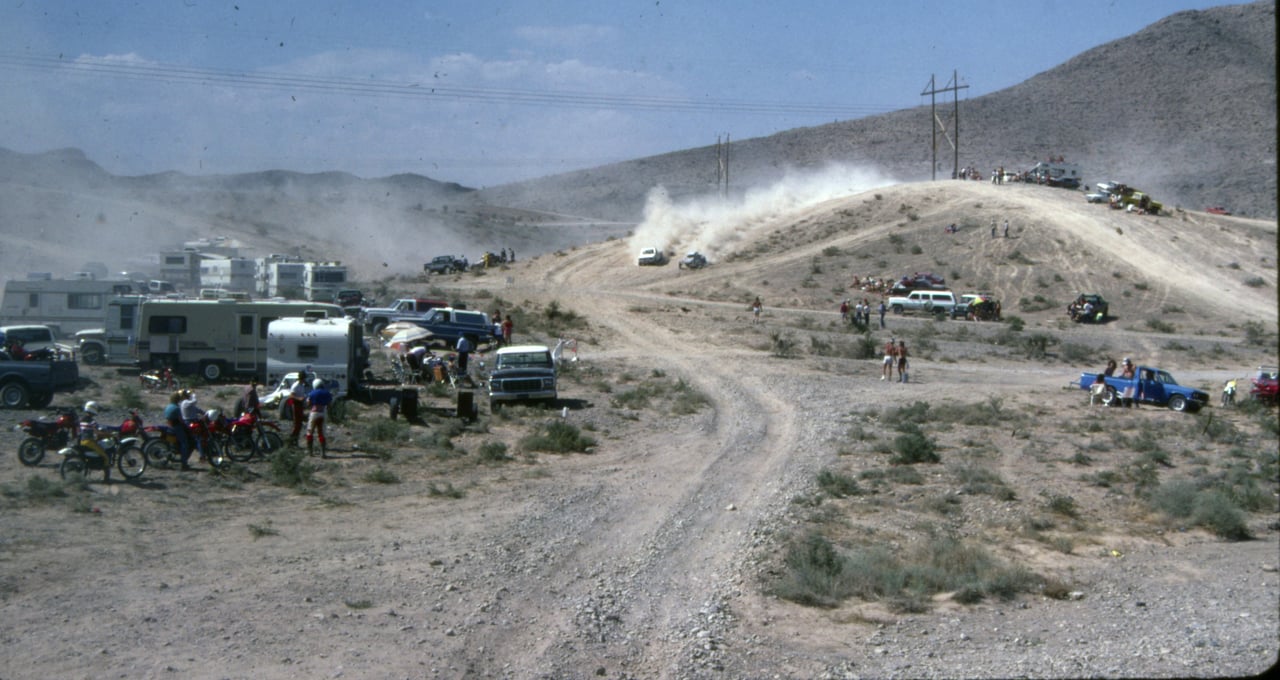 Race vehicles throw dust over a rise past spectator camps at the 1985 Mint 400 in the Nevada desert, photo by BLM Nevada