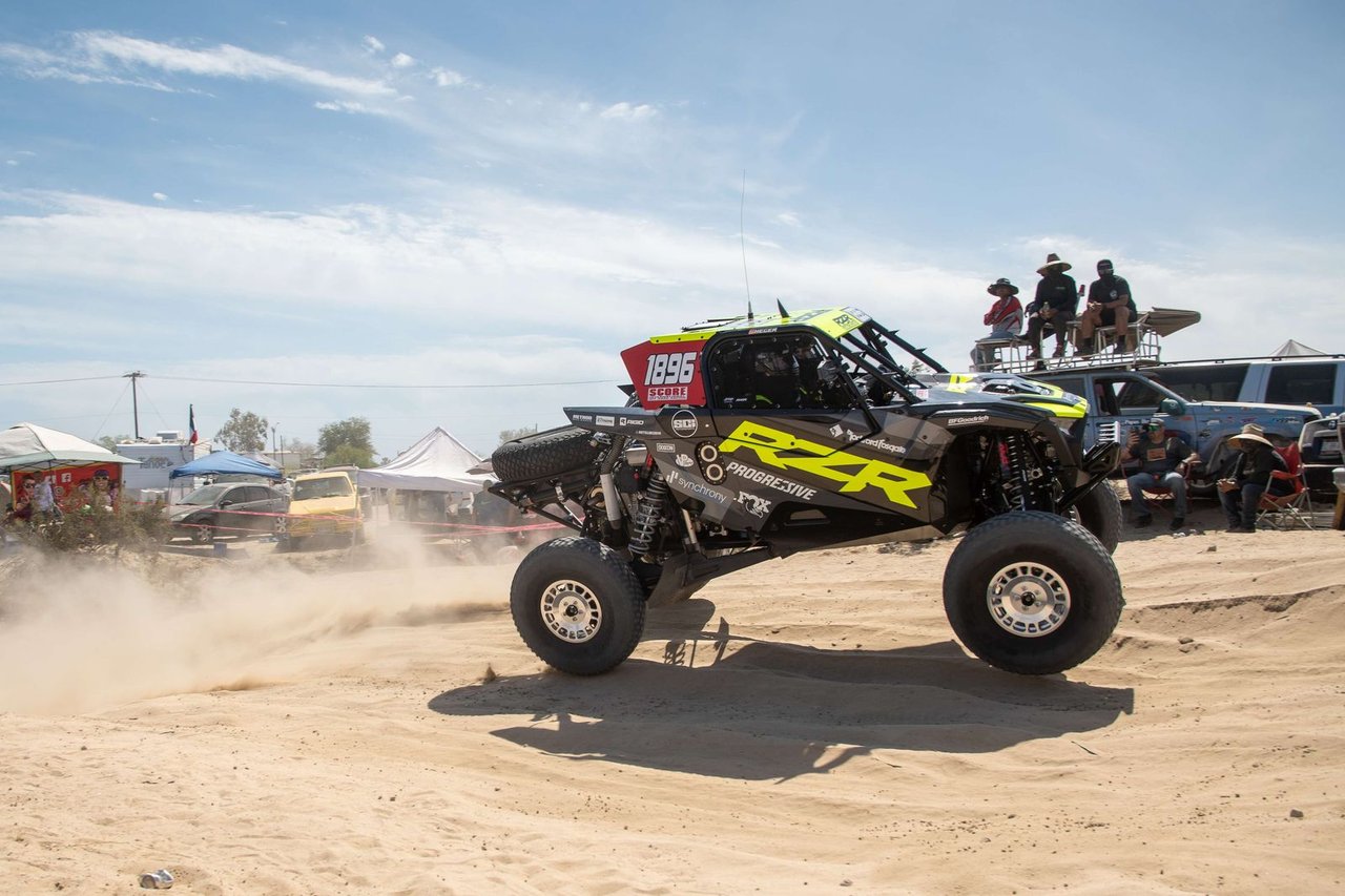 The No. 1896 Polaris RZR lifting its front tires off the sand as fans watch from a rooftop stand