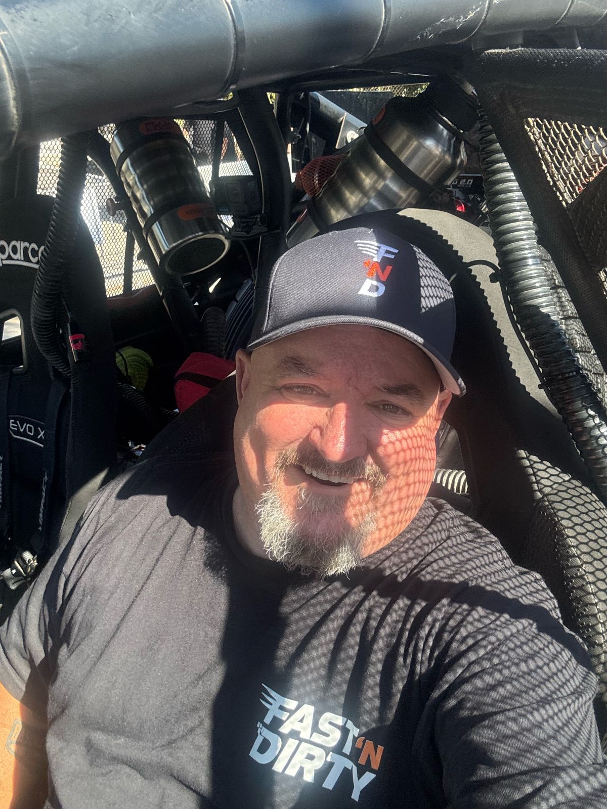 Brad in the seat of the Fast 'N Dirty UTV, the window net casting a checkerboard shadow across his face, at NORRA 500 tech in Ensenada